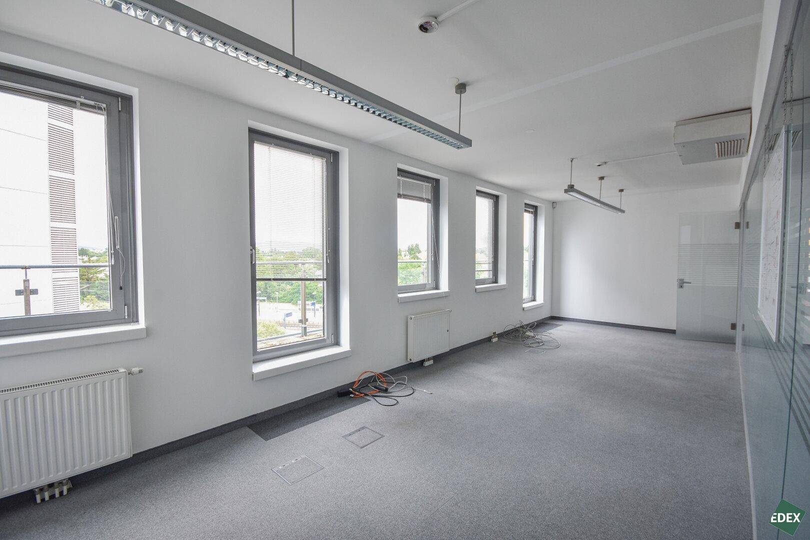 Langer Büroraum mit Teppichboden, vielen Fenstern und Blick nach draußen, bietet viel Tageslicht.