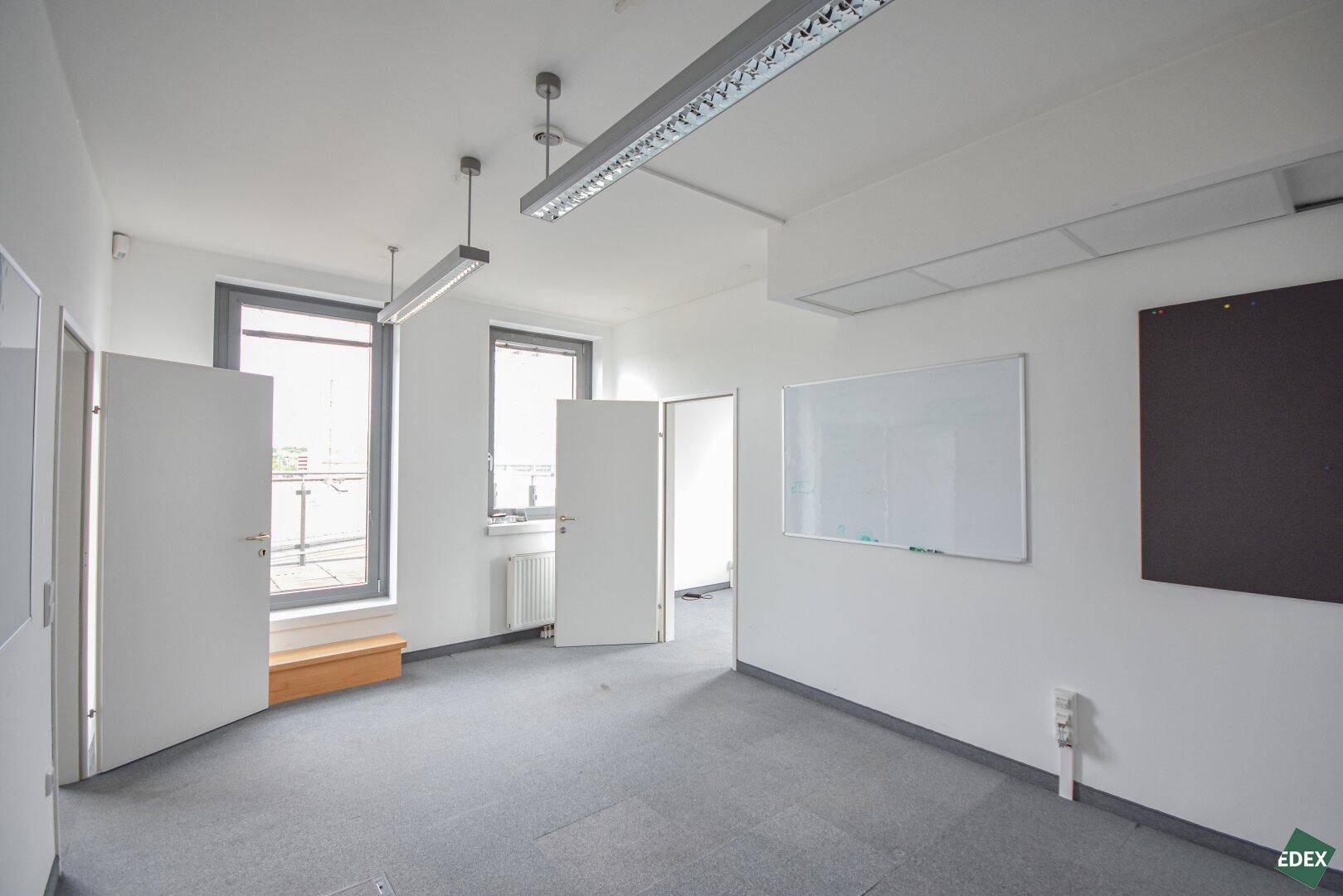 Bürofläche mit Teppichboden, mehreren Fenstern und Whiteboard an der Wand, bereit zur Nutzung.