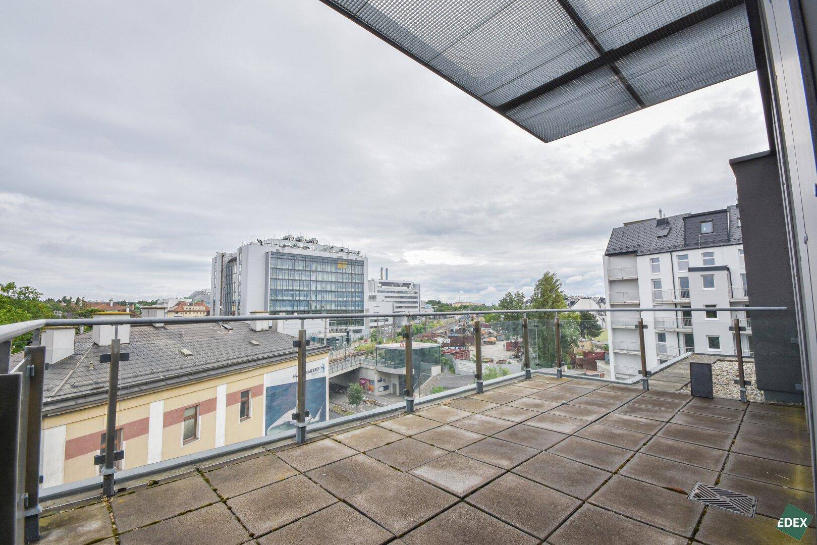 Große Dachterrasse mit Fliesenboden, Glasgeländer und Blick auf die Stadt, ideal zum Entspannen.