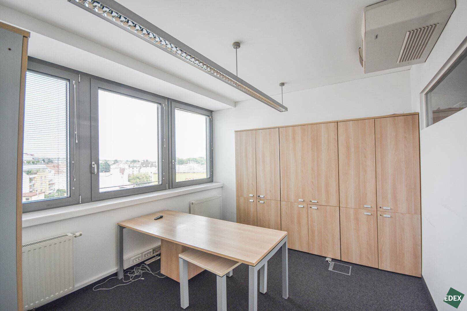 Einzelbüro mit Holzschränken, Schreibtisch und Blick nach draußen durch große Fenster.