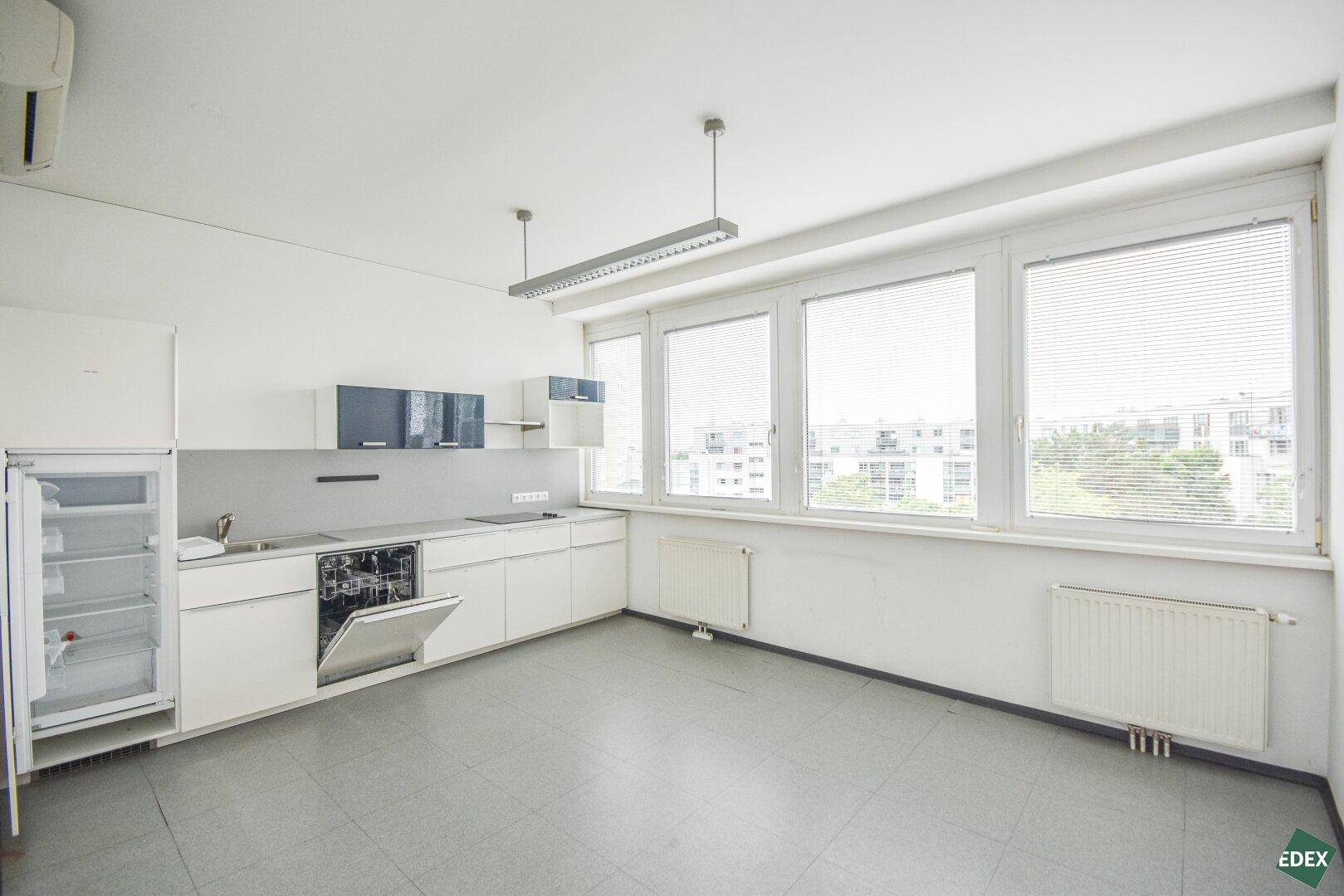 Helle Küche mit weißen Schränken, Fliesenboden und Blick auf die Stadt durch große Fenster.