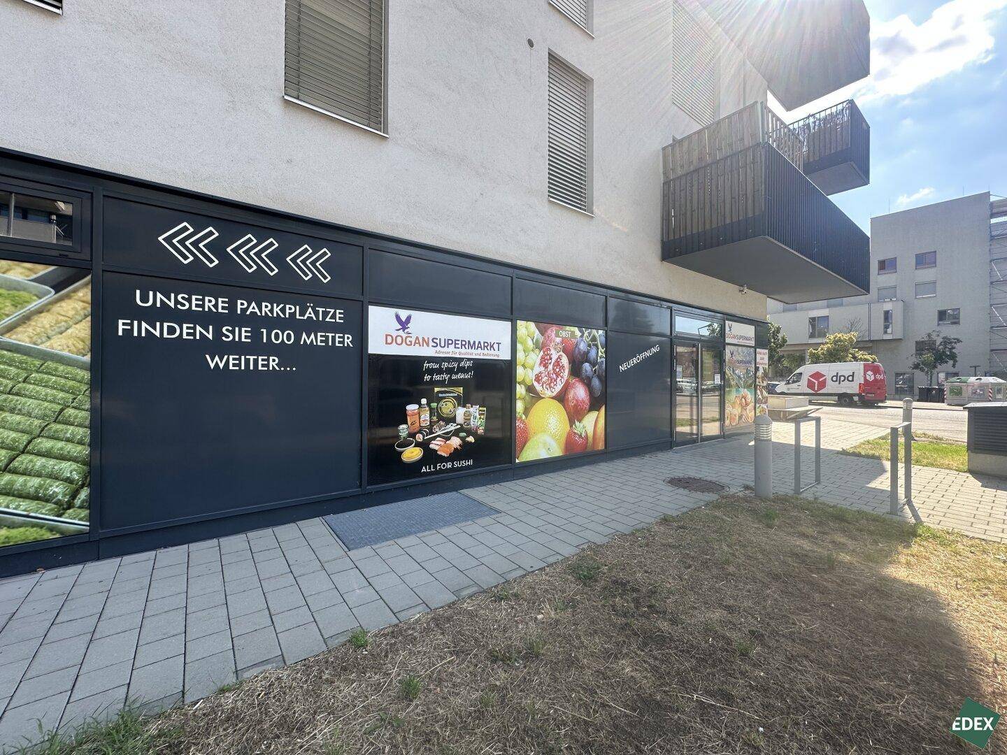 Ladenfronten eines Supermarktes im Erdgeschoss eines modernen Gebäudes mit Hinweisen zu Parkplätzen.
