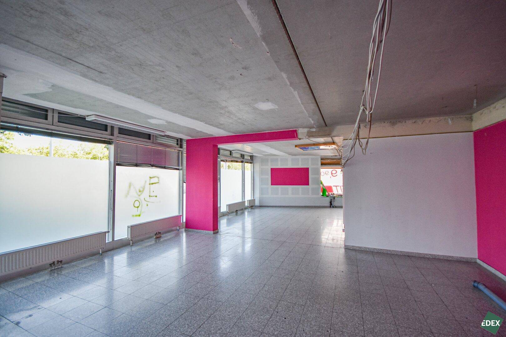 Gewerbefläche mit teilweise rosa gestrichenen Wänden, Milchglasfenstern und einer unverputzten Betondecke.