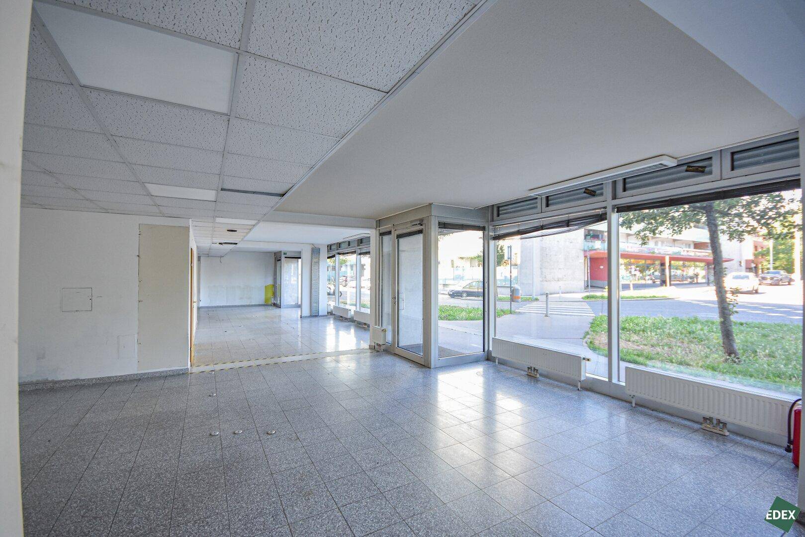 Heller und offener Gewerberaum mit Fliesenboden und großen Schaufenstern zur Straßenseite.