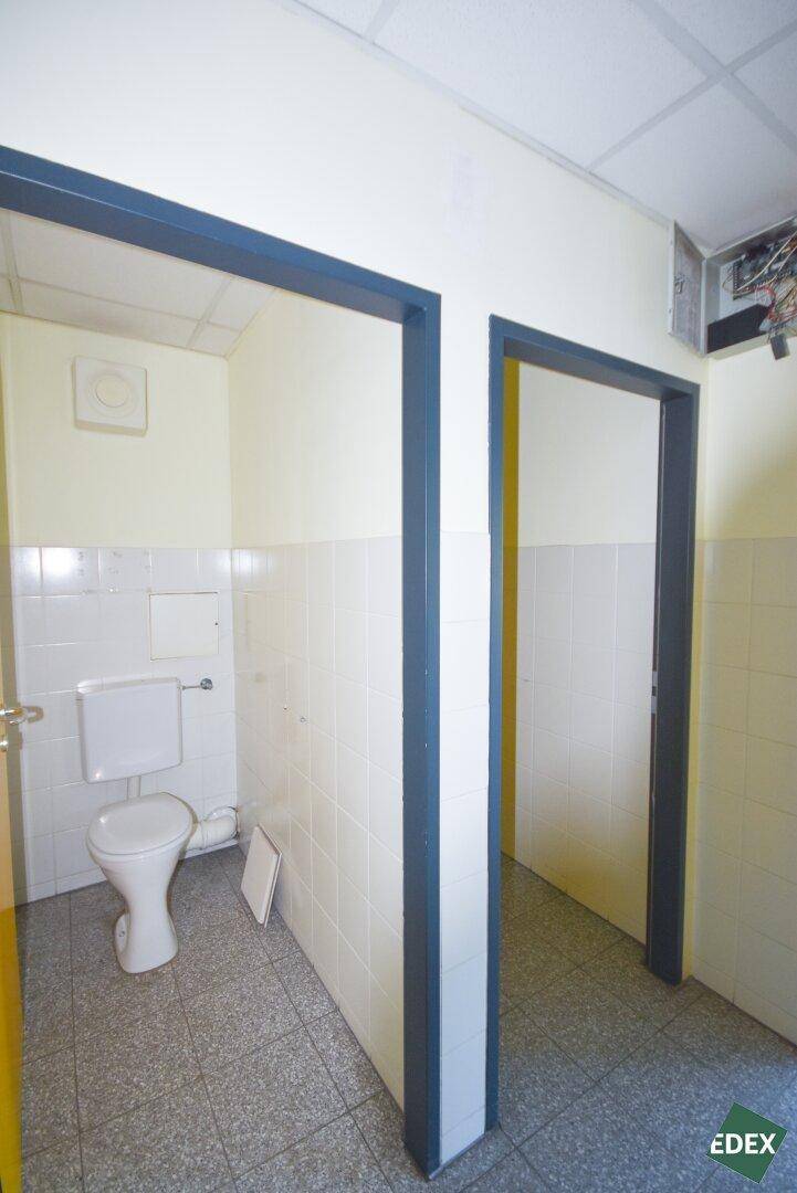 Toilettenraum mit wandhängendem WC, Abluftventilator und hellen Fliesen an Wänden und Boden.