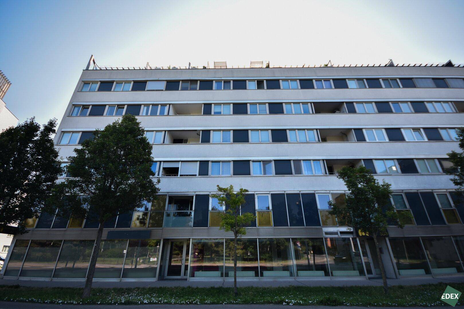 Gesamtansicht des modernen Gebäudes mit mehreren Stockwerken, vielen Fenstern und klarem Himmel.