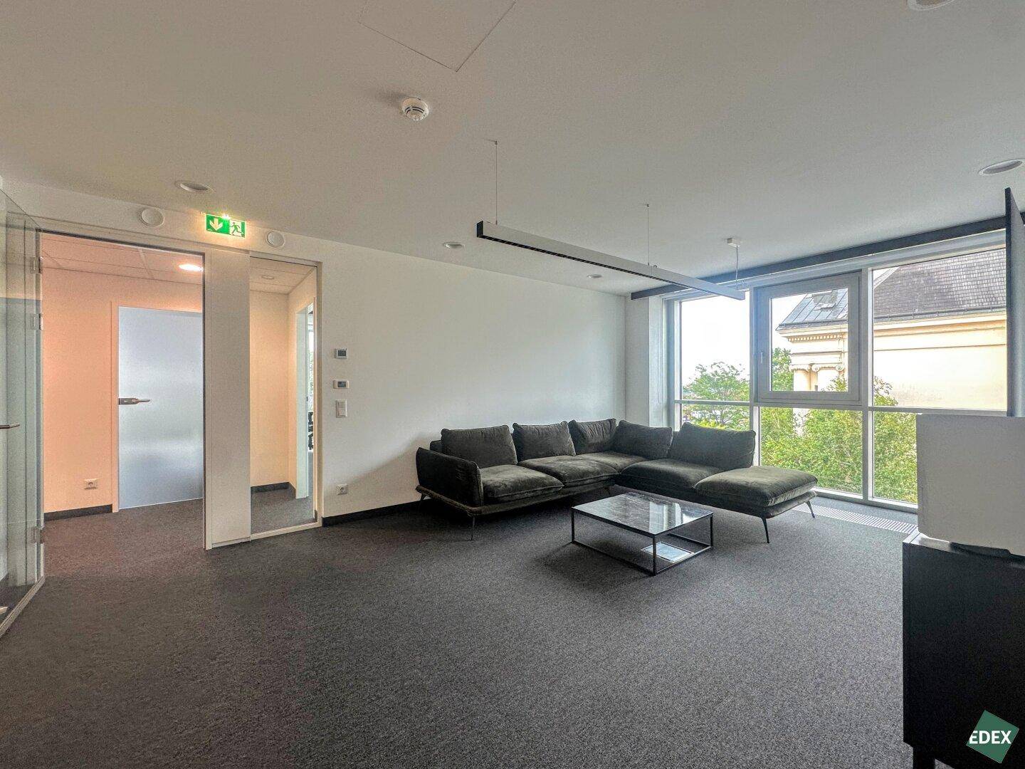 Gemütlicher Loungebereich mit großem Sofa, Glastrennwand und viel Tageslicht durch die Fenster.