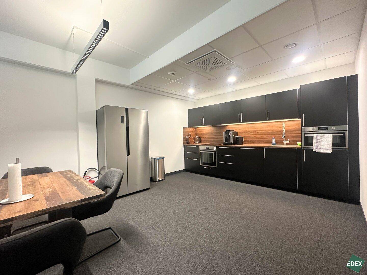 Moderne Küche mit dunklen Schränken, Holzakzenten, großem Kühlschrank und integrierten Geräten.