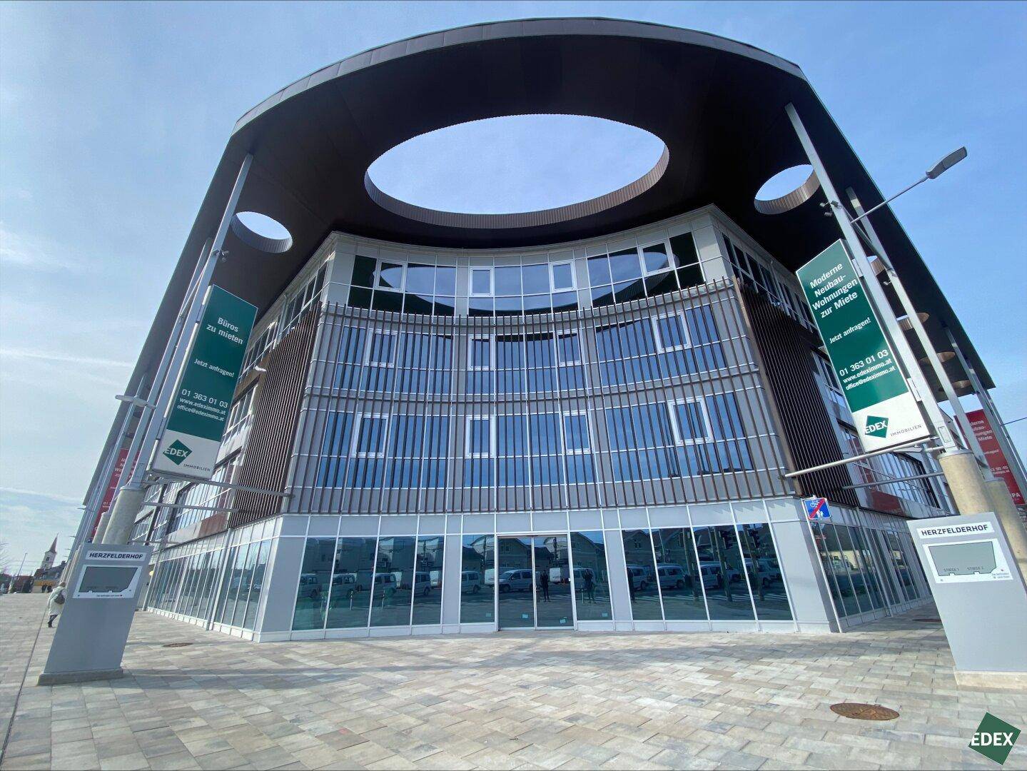 Modernes, geschwungenes Gebäude mit großer Glasfassade und einzigartigem Dachdesign in städtischer Umgebung.