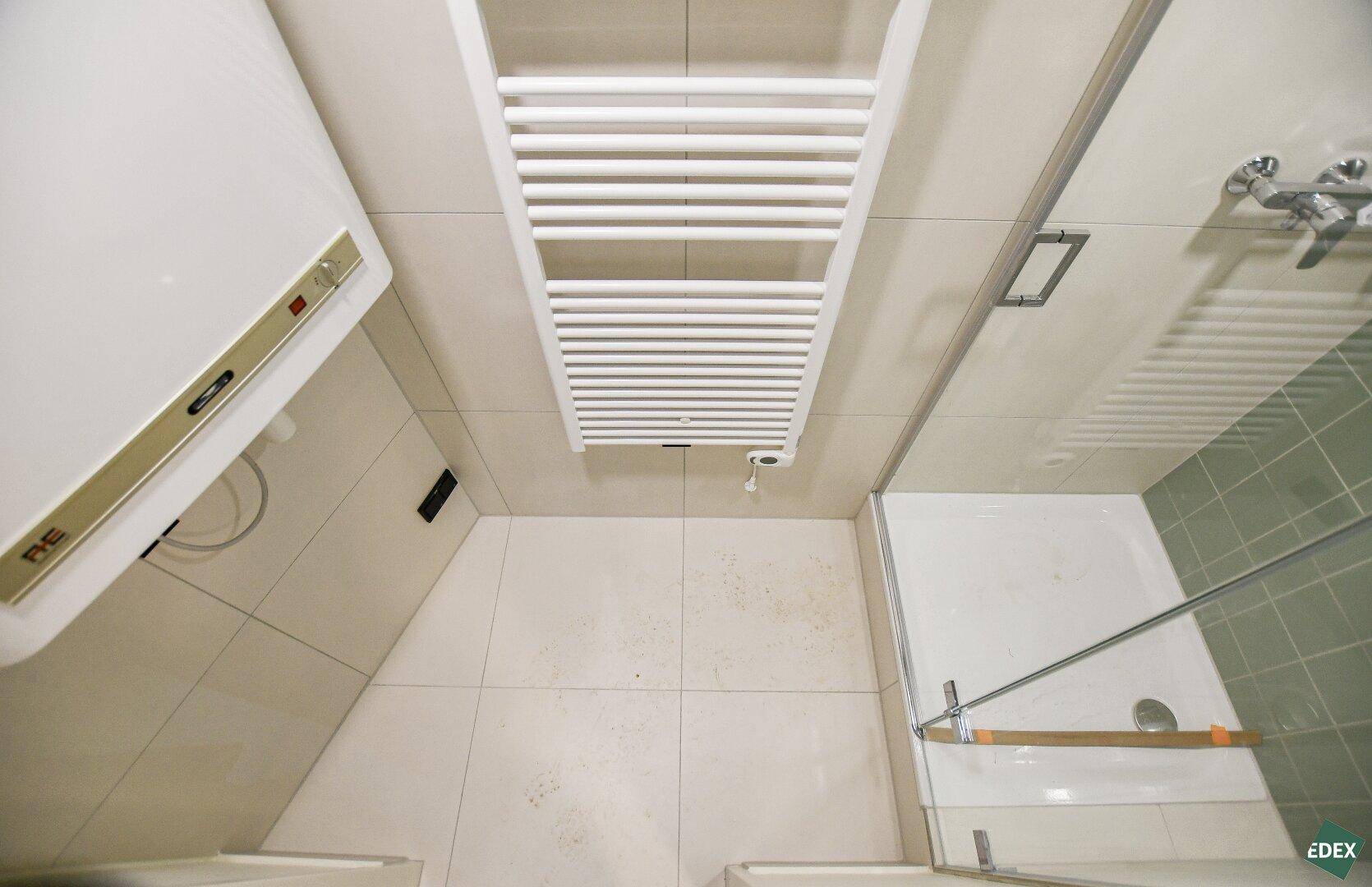 Ansicht von oben auf ein Badezimmer mit Duschkabine, Handtuchheizkörper und Fliesenboden.