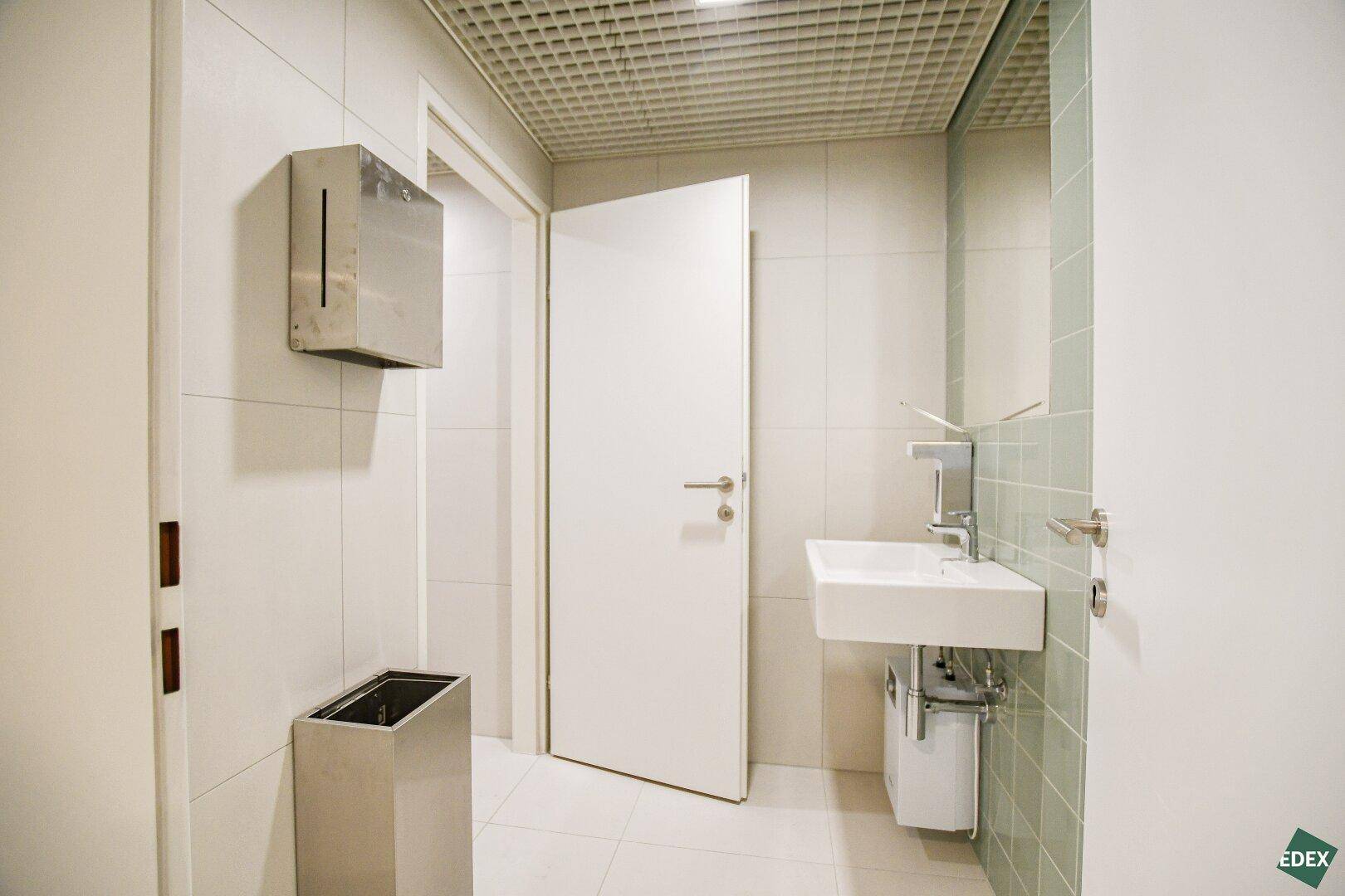 Modernes Badezimmer mit Waschbecken, Spiegel und weiß-grünen Fliesen, sauber und funktional.