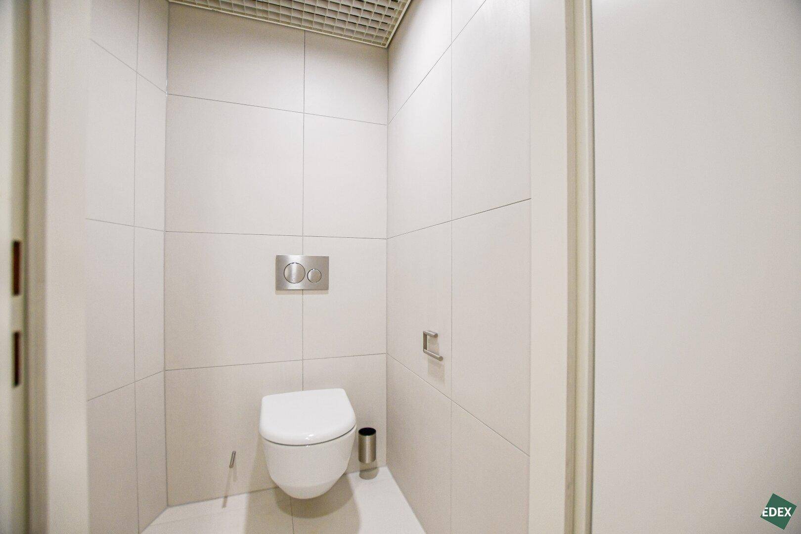 Separate Toilette mit Wand-WC und weißen Fliesen, minimalistisch und sauber gestaltet.