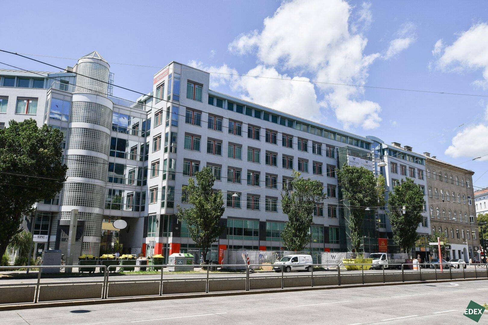 Modernes Bürogebäude mit Glasfassade und vielen Fenstern an einer belebten Straße.