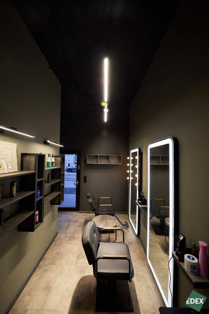 Friseursalon mit modernen Stylingstühlen, beleuchteten Spiegeln und Produktregalen in dunkler Farbgebung.