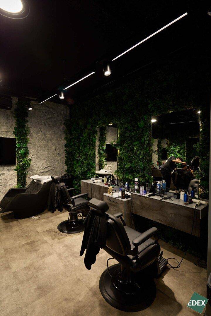 Ansicht des Friseurbereichs mit mehreren Stylingstühlen, großen Spiegeln und der markanten grünen Wandgestaltung.