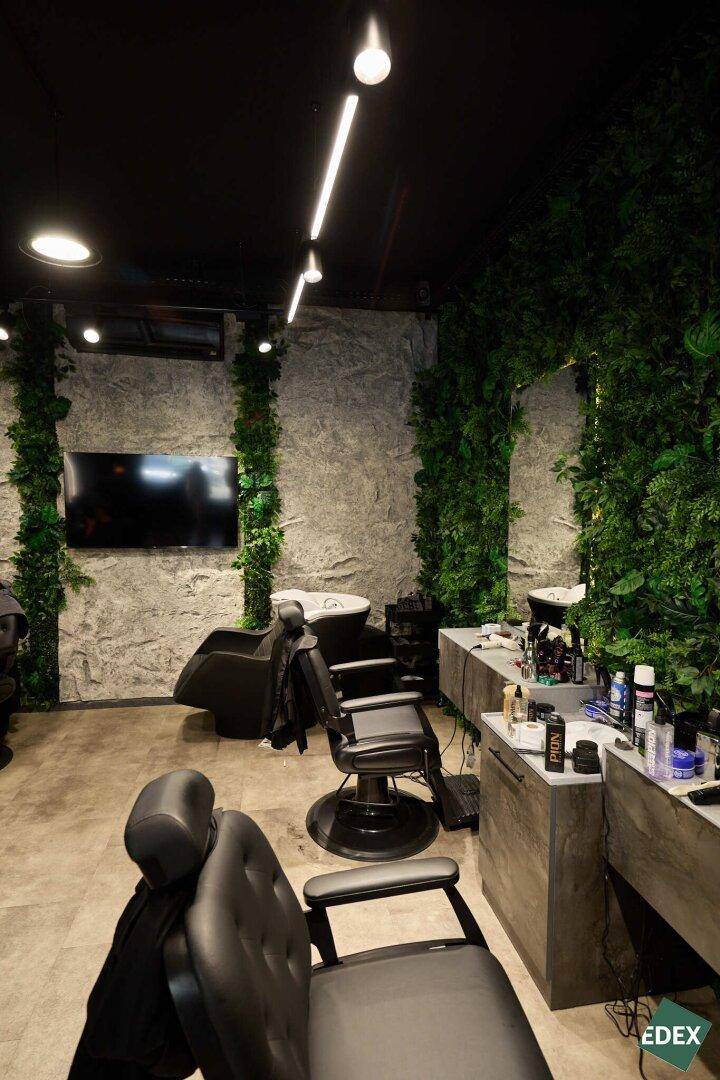 Übersicht des Friseurbereichs mit Stylingstühlen, Waschbecken und der Kombination aus Steinwand und vertikalen Pflanzen.