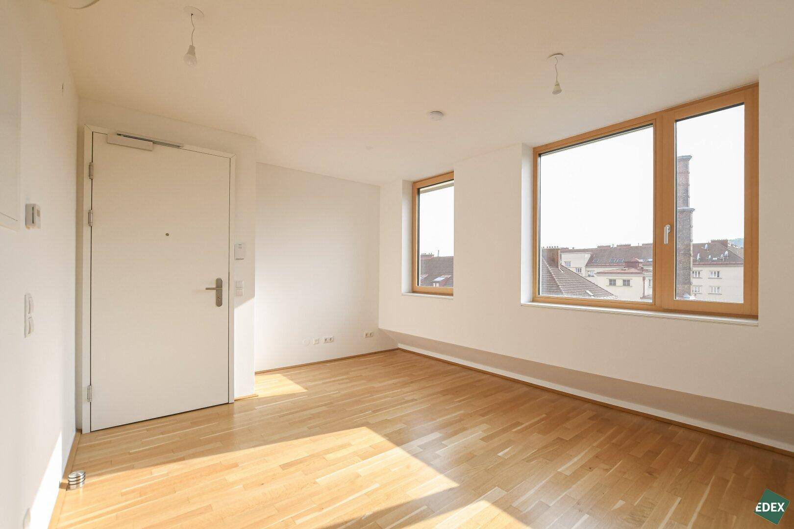 Helles, leeres Zimmer mit Parkettboden und großen Fenstern, bereit zur individuellen Gestaltung.