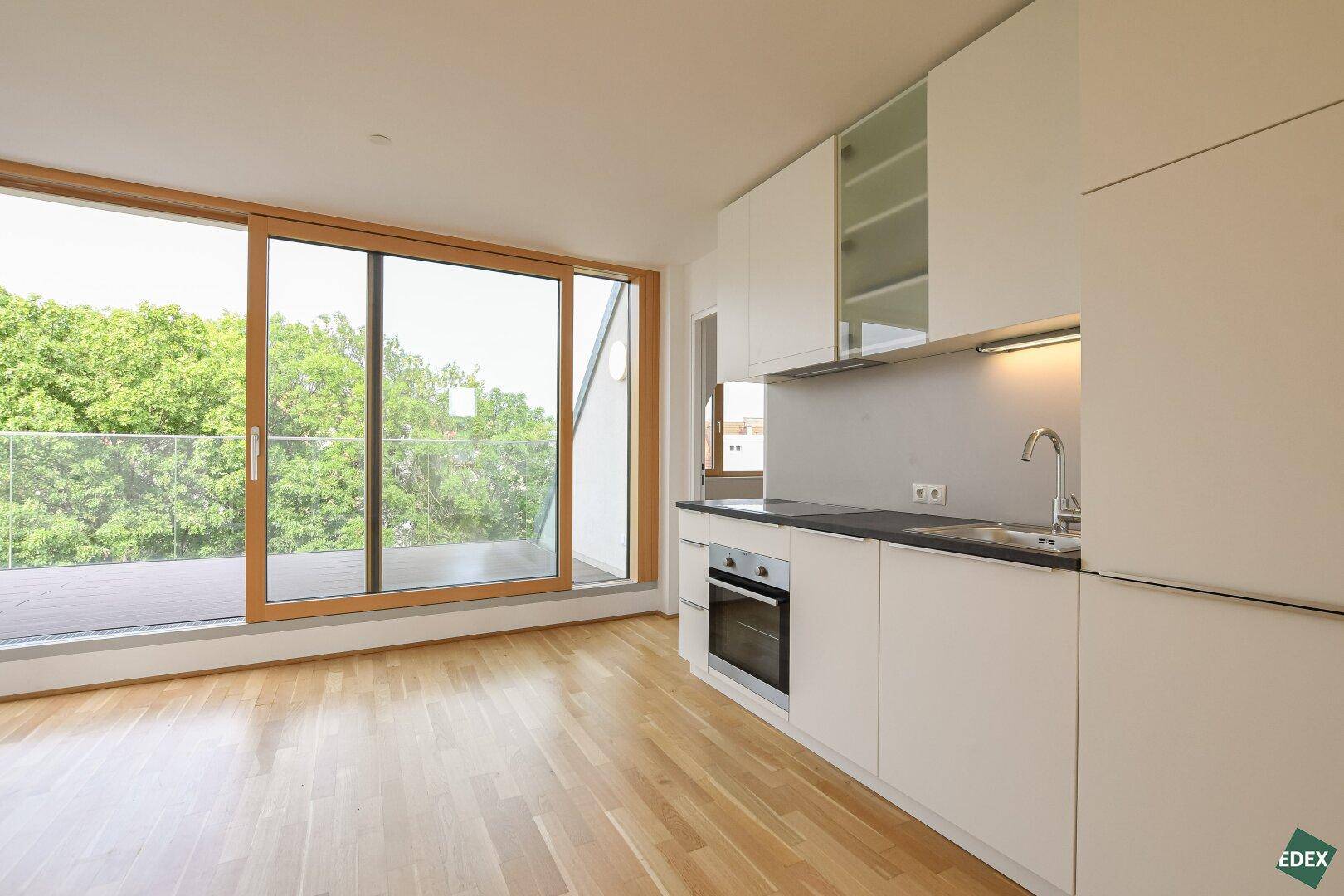 Moderne Küchenzeile mit weißen Schränken und Zugang zu einer großen Terrasse mit Grünblick.