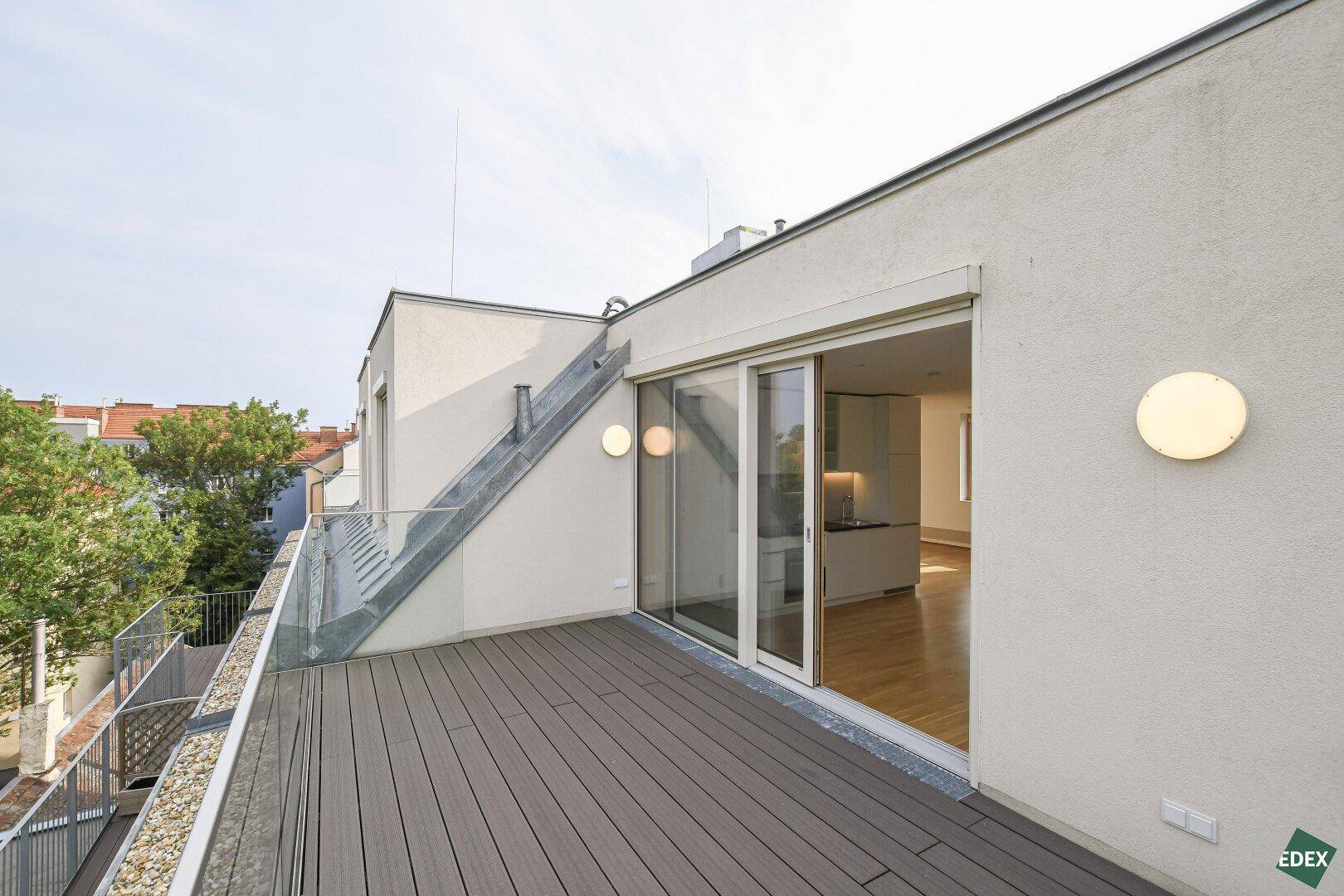 Geräumige Dachterrasse mit Holzboden und Blick auf die umliegenden Gebäude und Bäume.