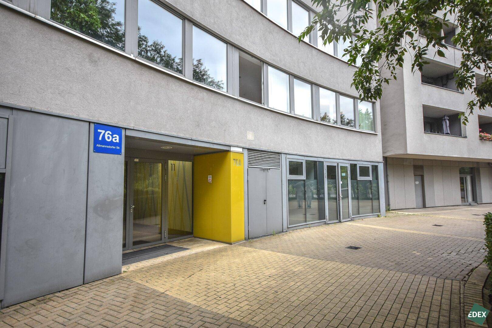 Eingangsbereich eines modernen Bürogebäudes mit Hausnummer 76a und gelber Akzentwand.