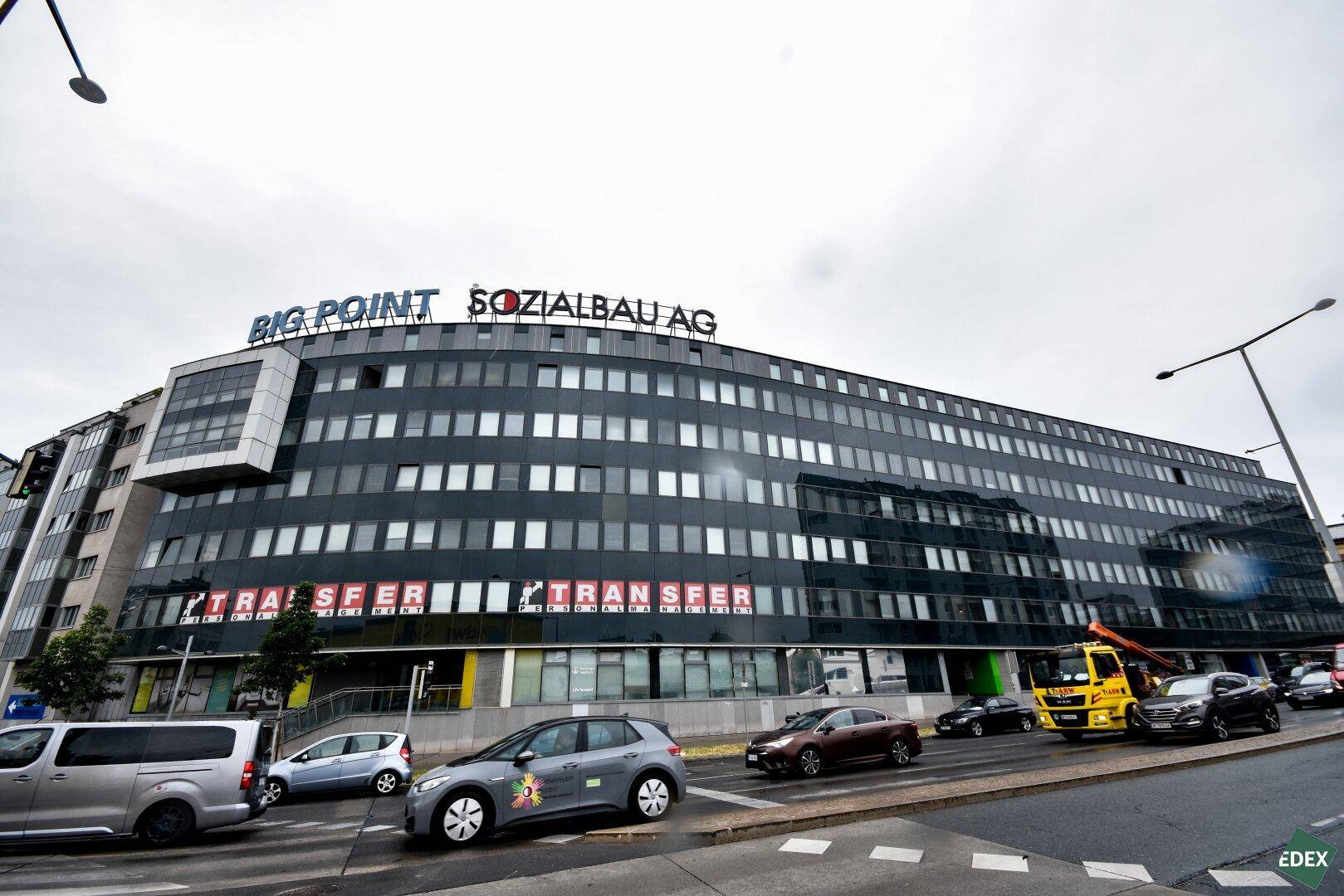 Großes Bürogebäude "Big Point" an einer belebten Straße mit vielen Autos und einem grauen Himmel.
