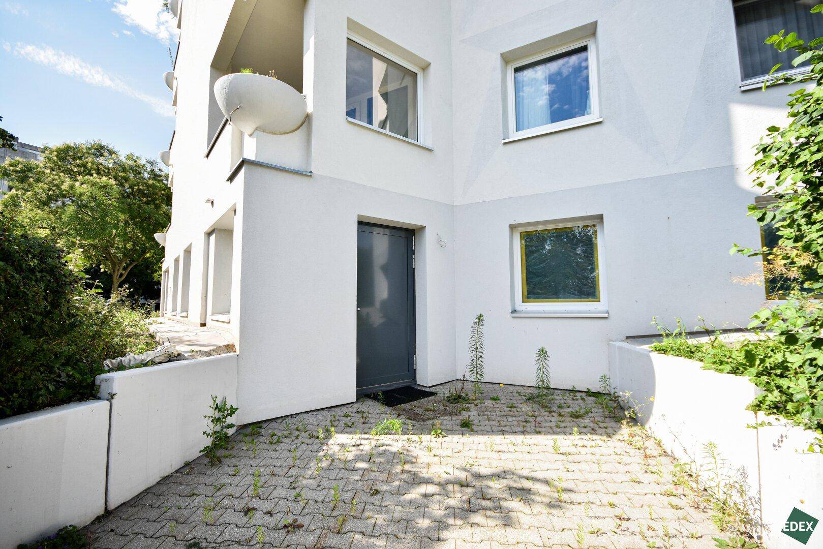 Kleiner gepflasterter Außenbereich am Eingang eines modernen Mehrfamilienhauses mit Grünflächen.