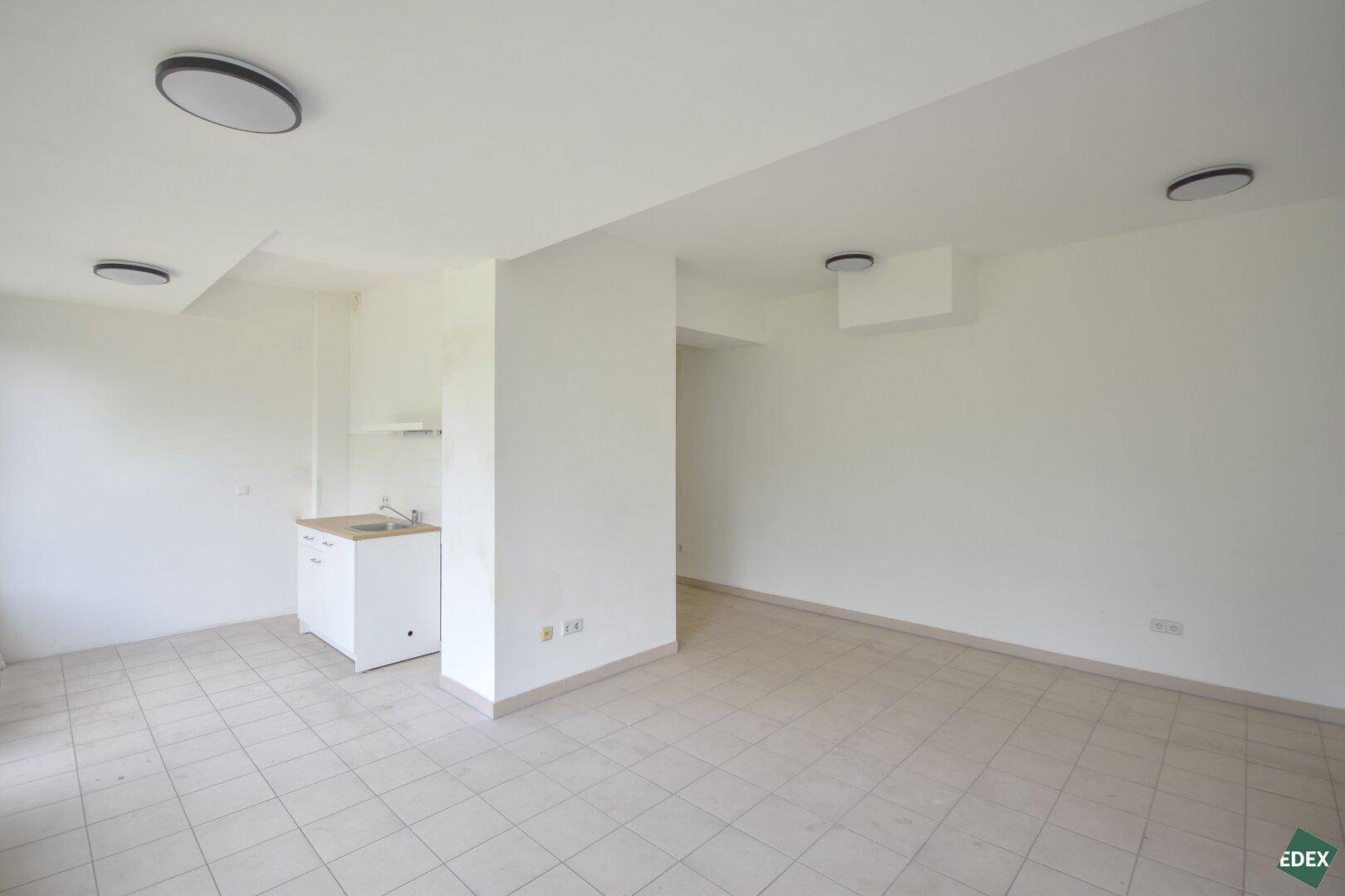 Heller Raum mit integrierter Küchenzeile und Fliesenboden, ideal für eine kleine Wohnung oder Büro.