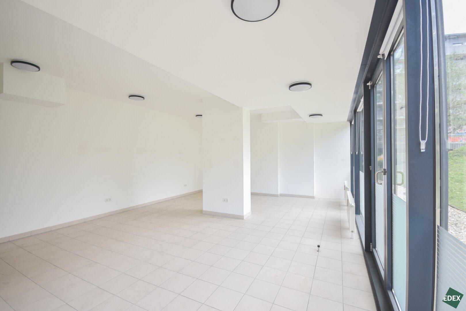 Langer, heller Raum mit durchgehenden Fenstern und Fliesenboden, bietet viel Platz und Tageslicht.