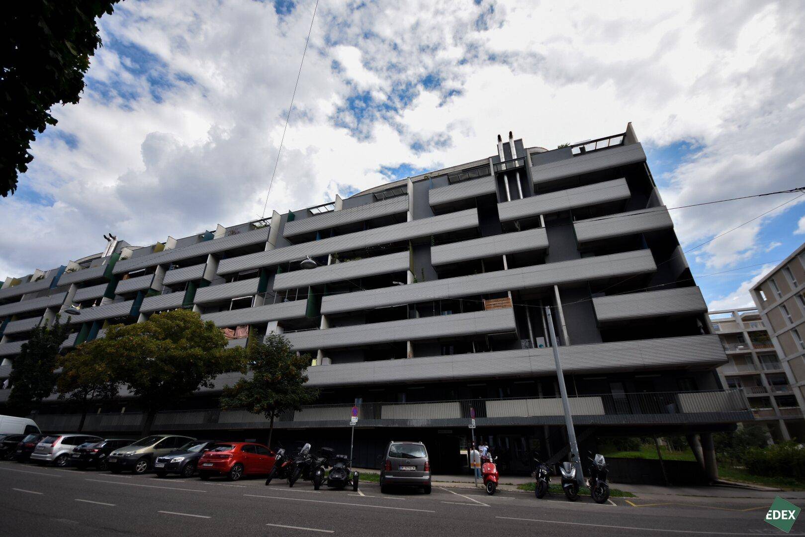 Moderne Architektur des Gebäudes mit zahlreichen Balkonen und einer markanten Fassade, von der Straße aus gesehen.