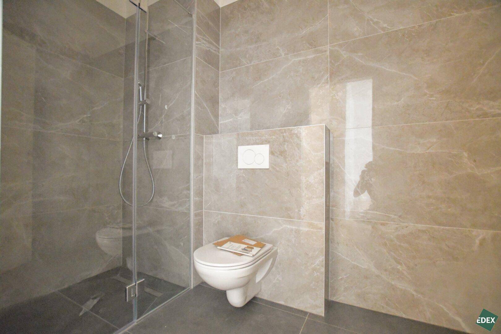 Modernes Badezimmer in neuwertigem Zustand mit begehbarer Dusche und Wand-WC, ausgestattet mit großformatigen Fliesen.