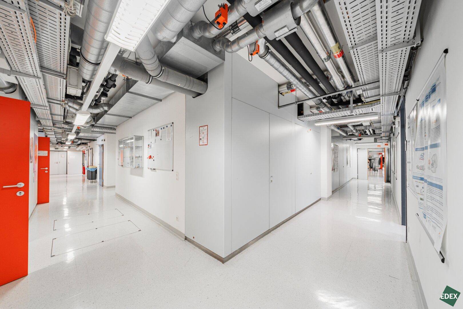 Langer Flur mit sichtbaren Lüftungsrohren und Kabeltrassen an der Decke.