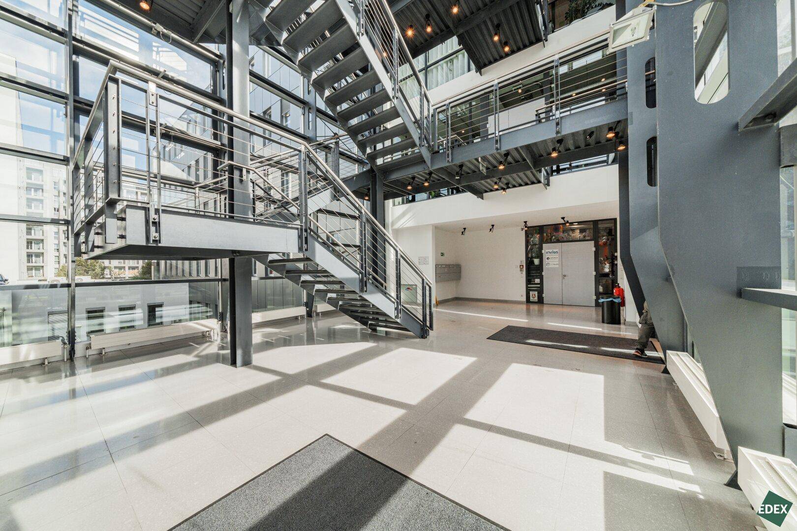 Geräumige Lobby mit moderner Metalltreppe, Glasfassade und hellem Fliesenboden.