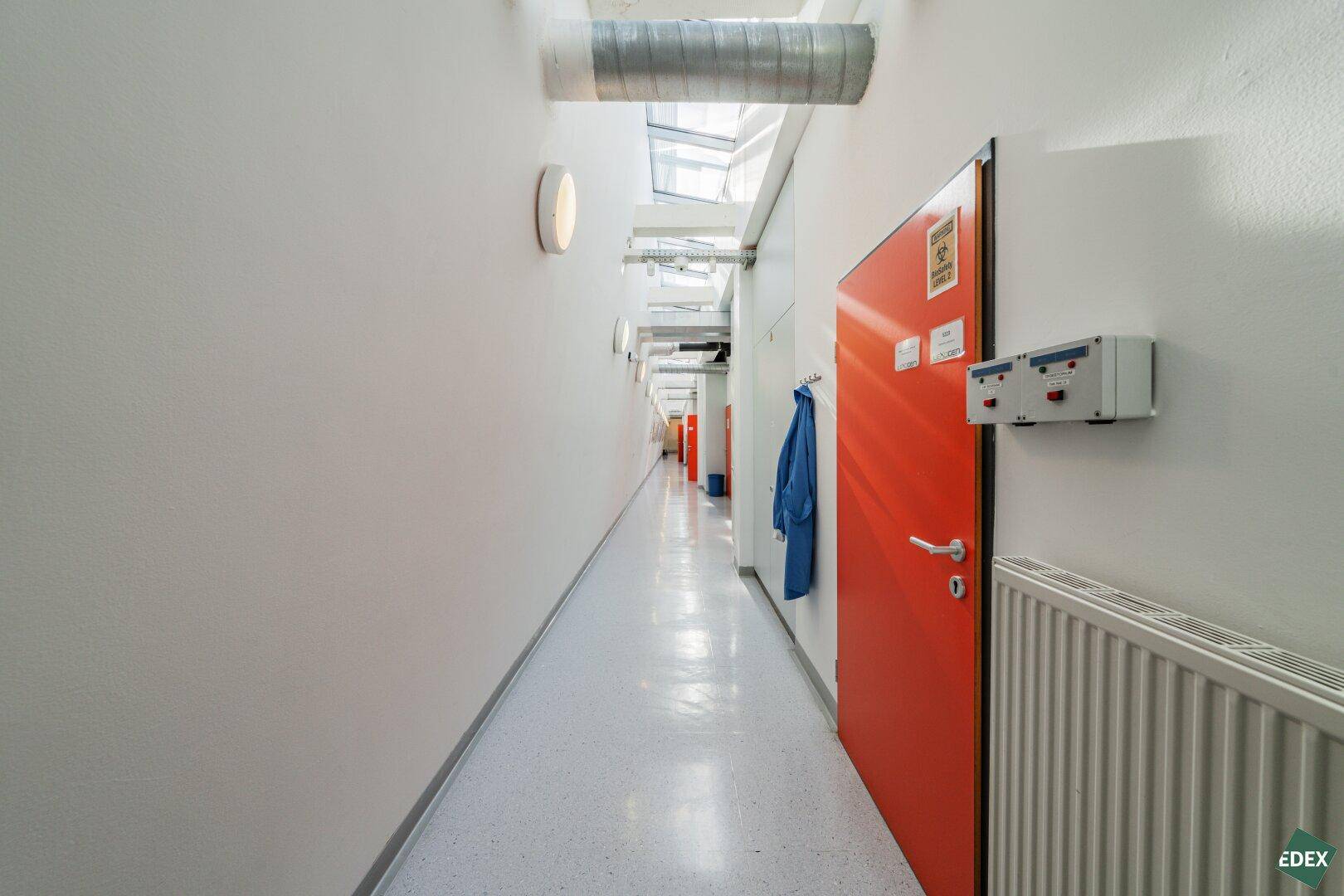 Langer, schmaler Flur mit weißen Wänden, roter Tür und Heizkörper.
