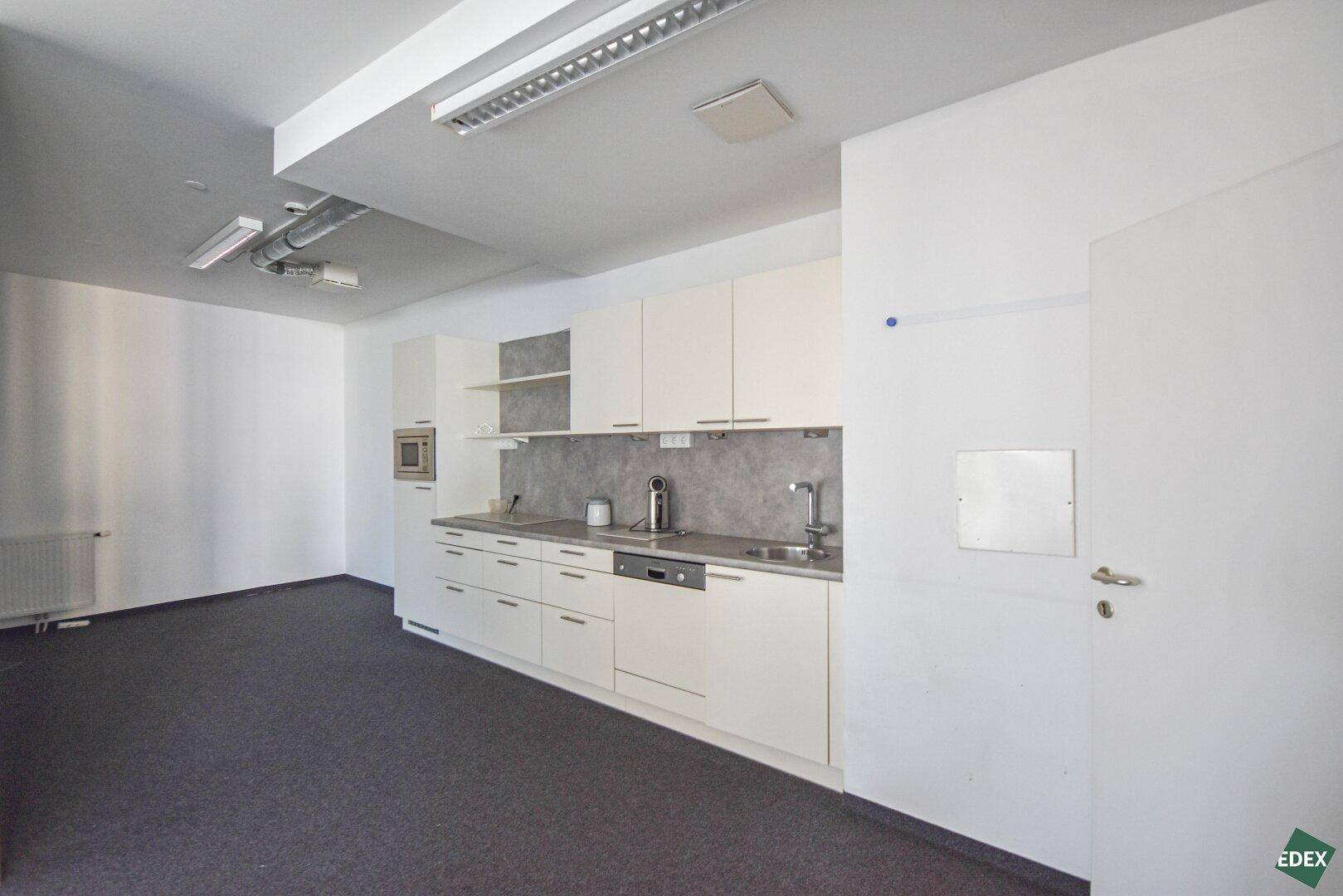 Moderne Küchenzeile mit weißen Schränken, Spülmaschine und Mikrowelle in einem Bürobereich.