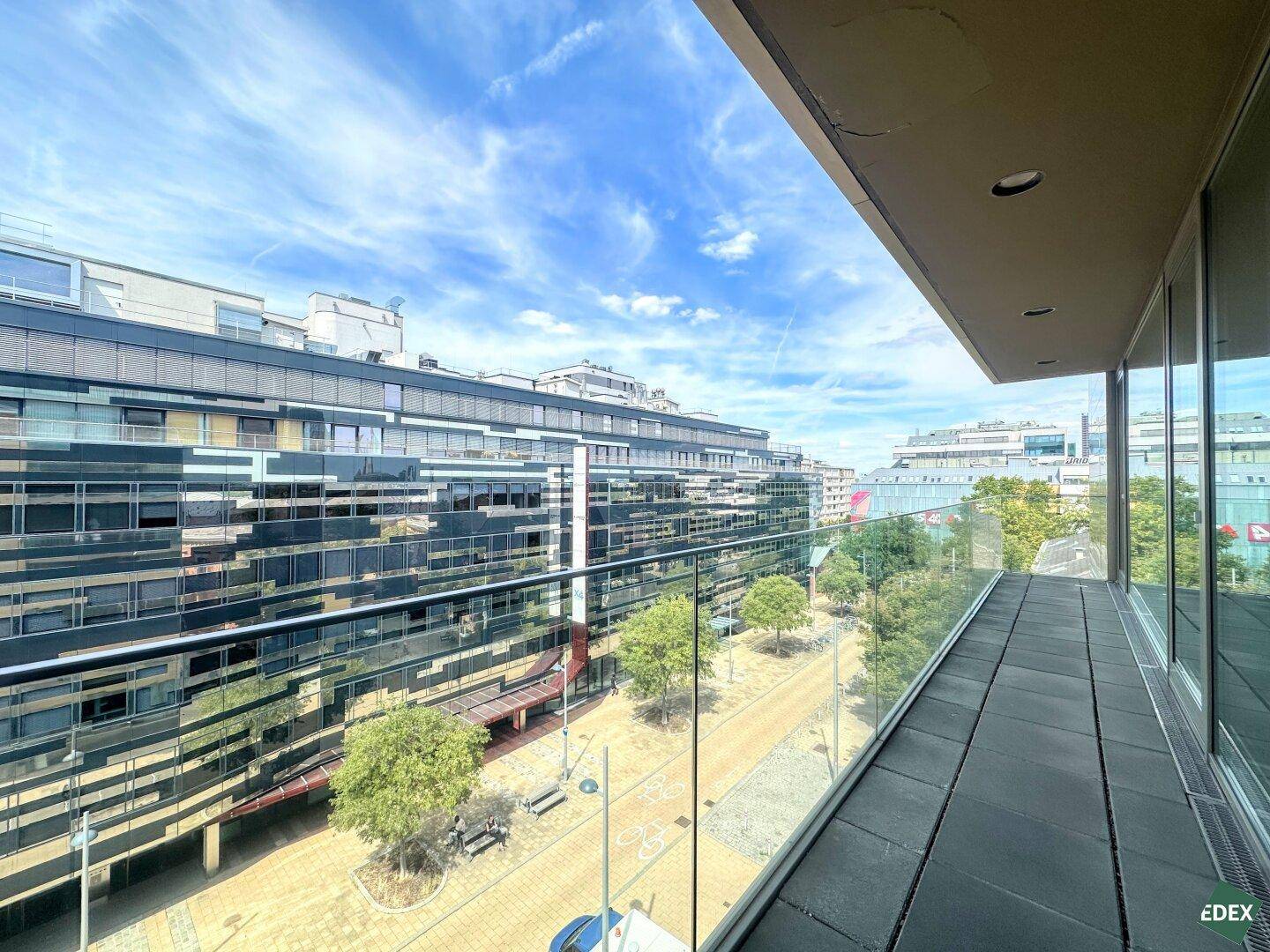 Moderner Balkon mit Glasbrüstung und Blick auf die umliegenden Gebäude und die Straße.