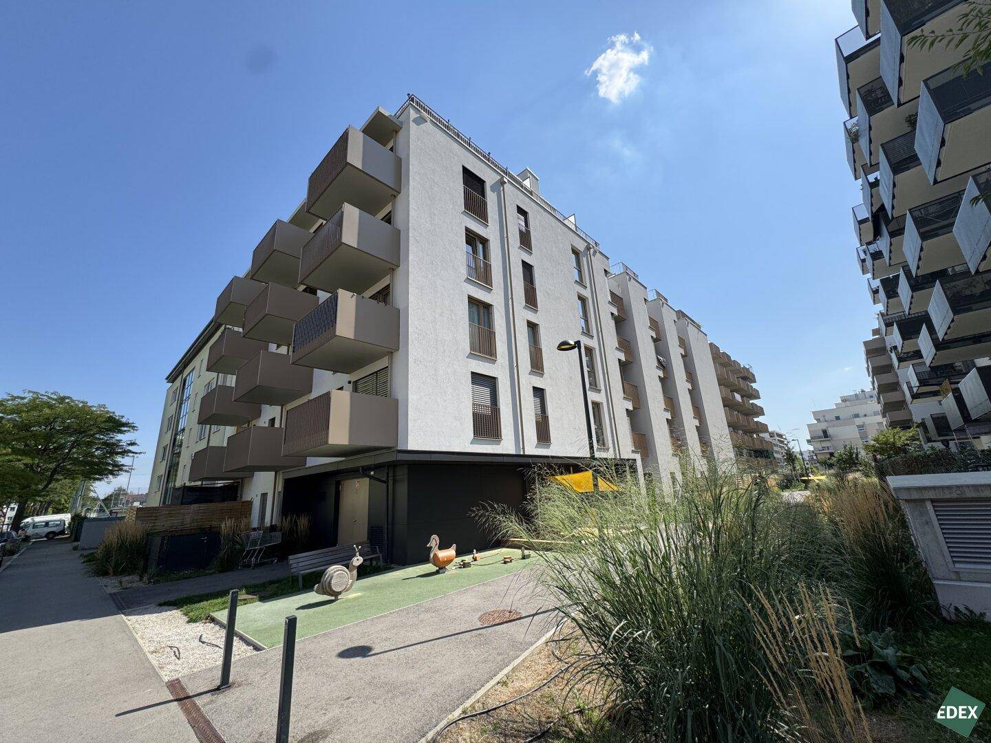 Moderne Wohnanlage mit zahlreichen Balkonen unter blauem Himmel und gepflegter Außenanlage.