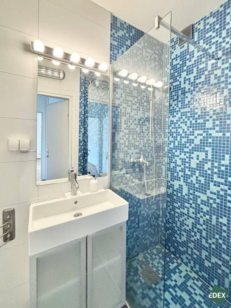 Modernes Badezimmer mit blauen Mosaikfliesen in der Dusche und einem Waschbecken mit Spiegel.