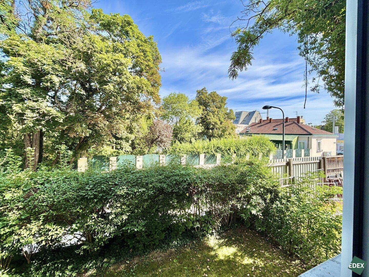 Grüner Ausblick auf Bäume und Hecken von einem Fenster oder Balkon.