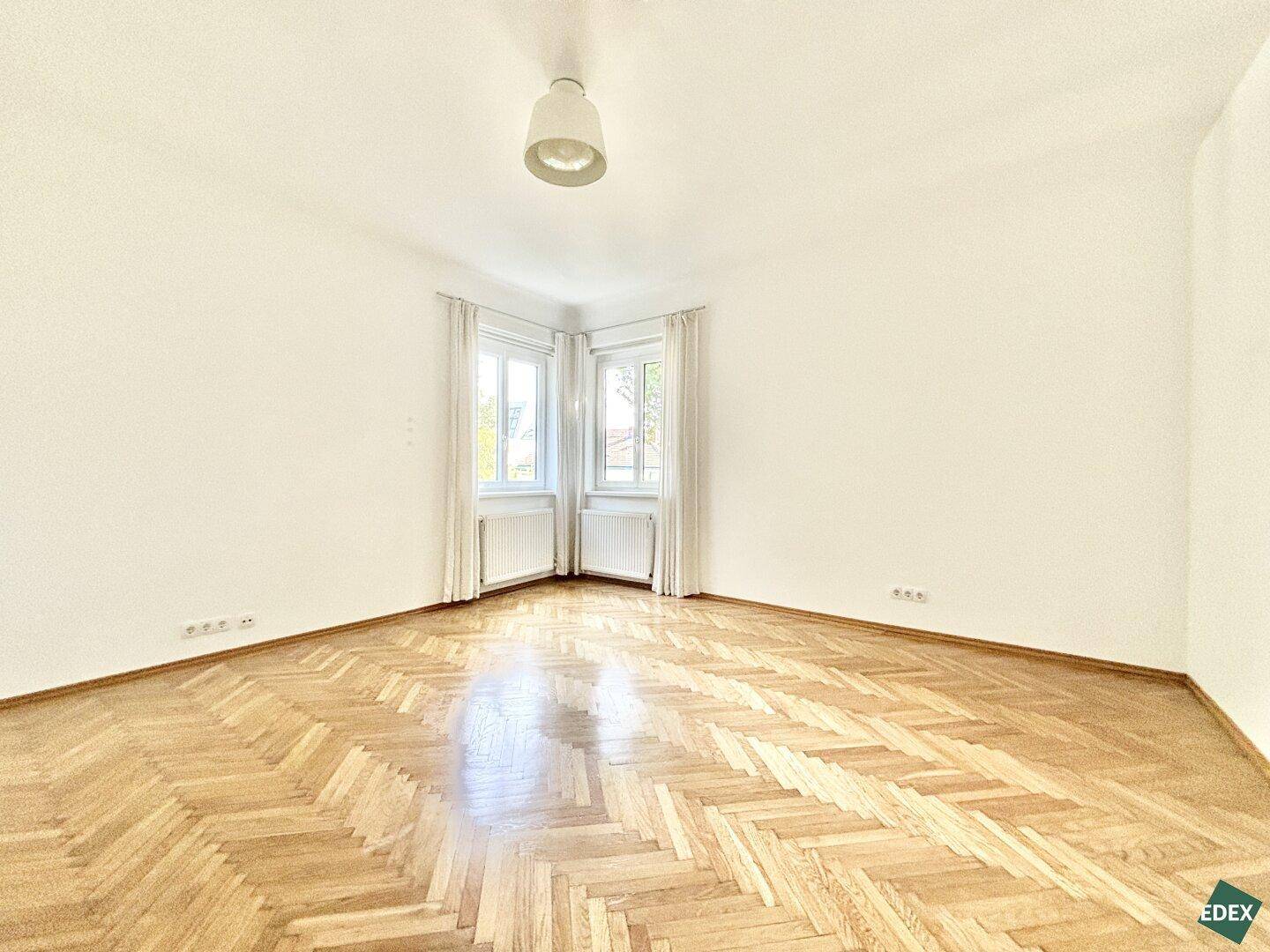 Leeres Zimmer mit Fischgrätparkettboden und hellen Wänden, bereit zur Einrichtung.