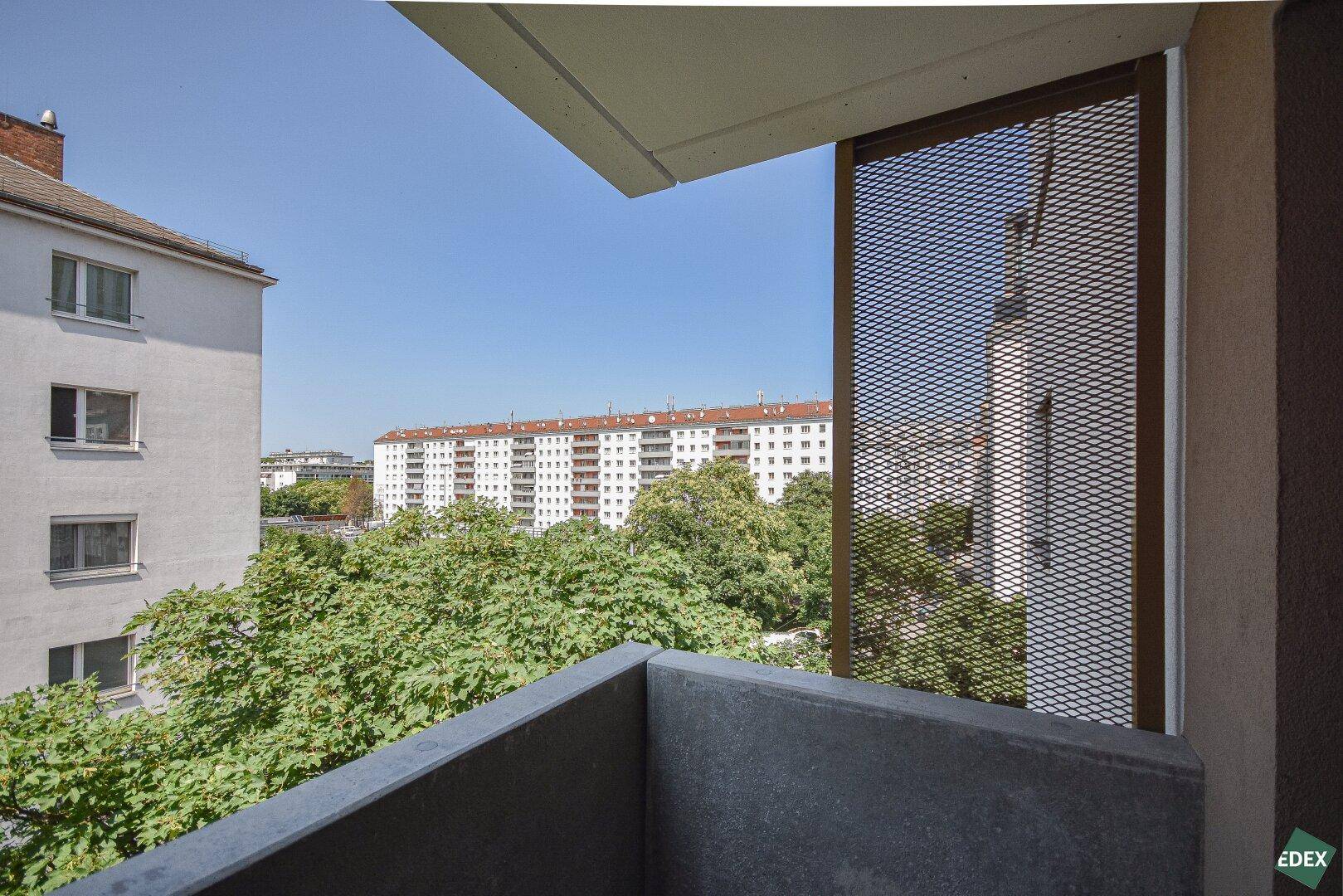 Ausblick vom Balkon auf grüne Bäume und umliegende Wohngebäude in der Stadt.
