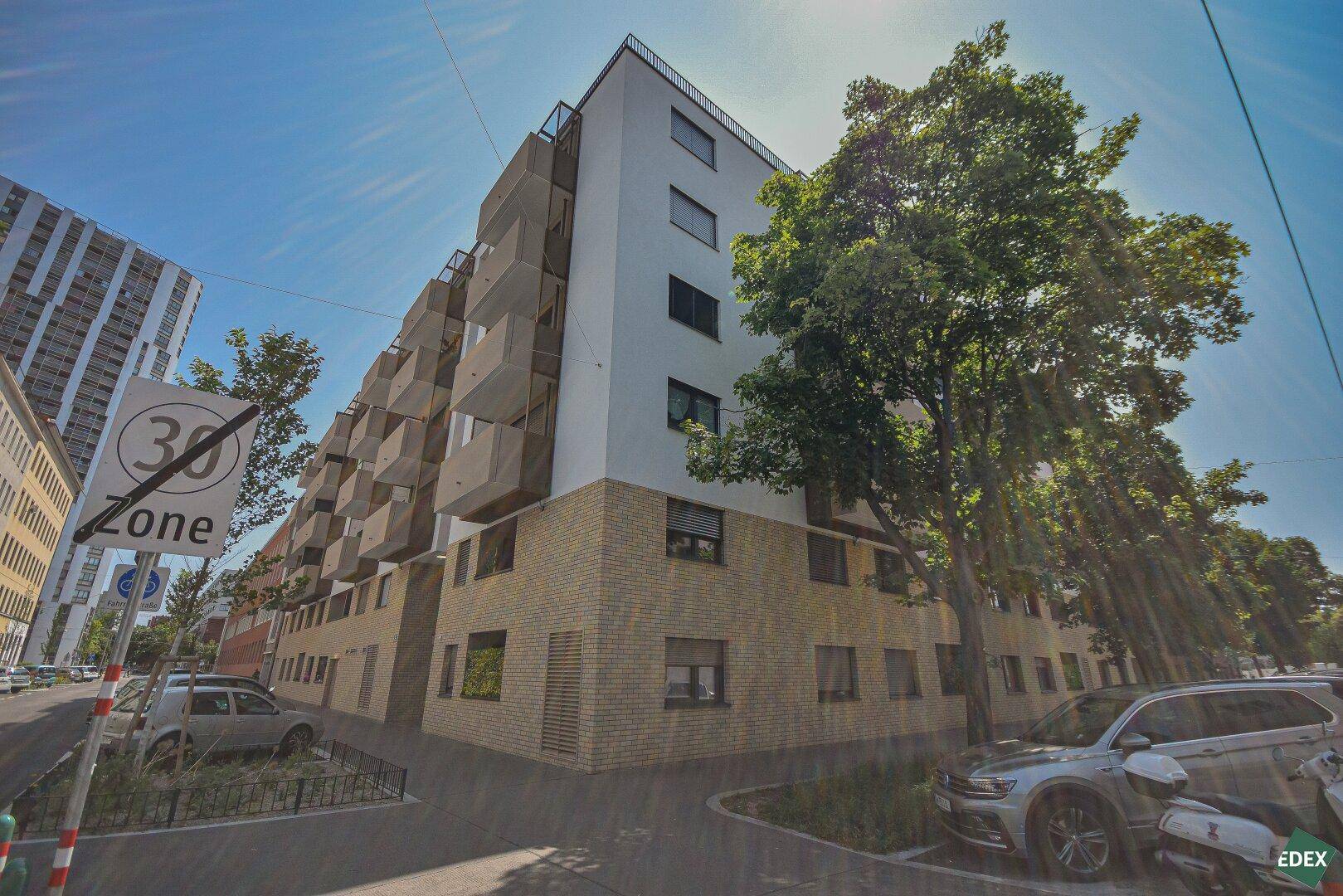 Moderne Wohnanlage mit Balkonen und Ziegelfassade, umgeben von Bäumen und Parkplätzen.