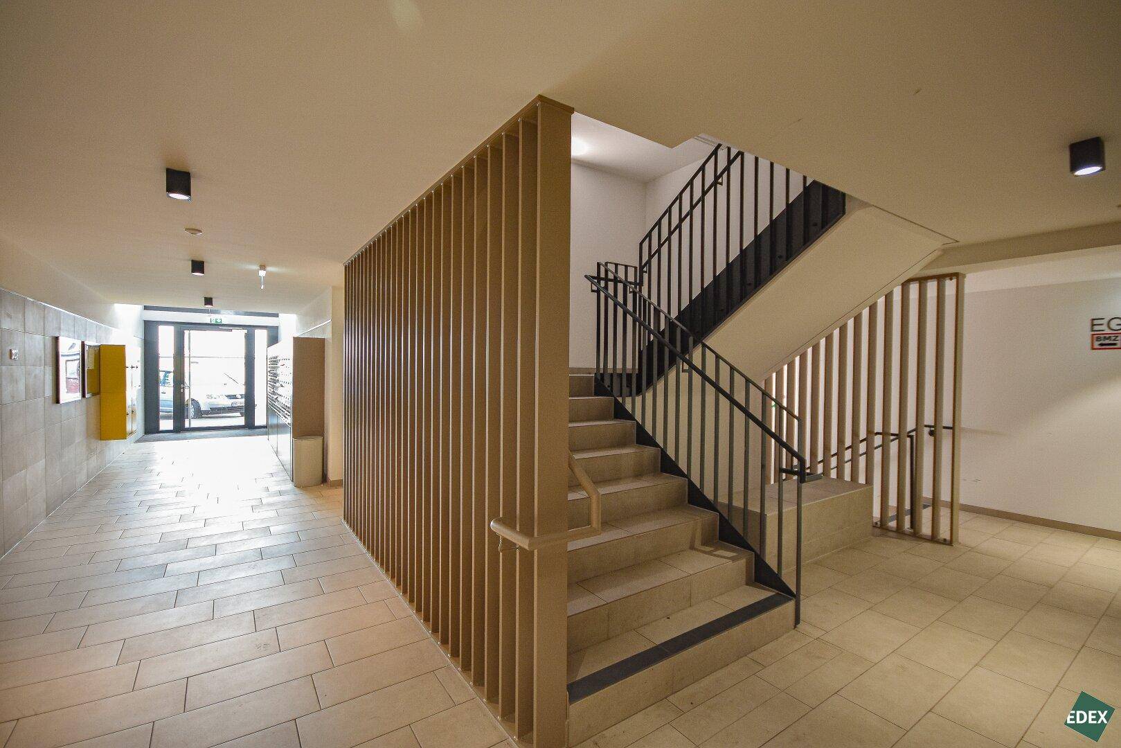 Heller Eingangsbereich mit Treppenhaus und modernen Holzlamellen, führt zu den Wohneinheiten.