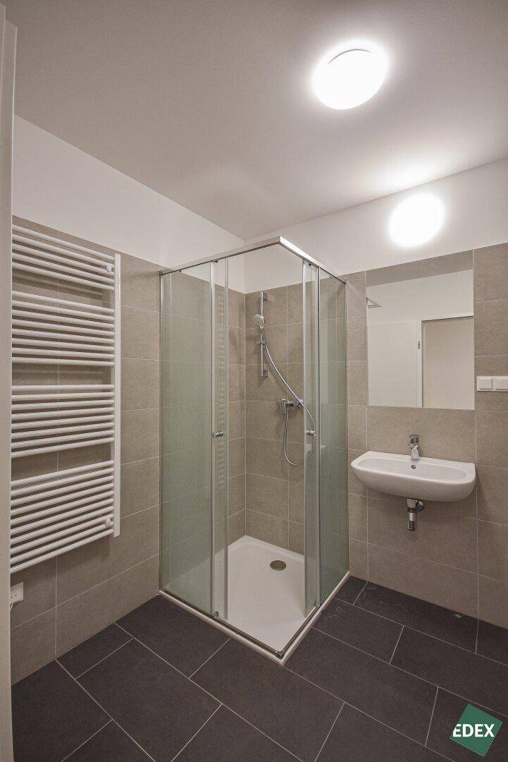 Modernes Badezimmer mit Eckduschkabine, Waschbecken und praktischem Handtuchheizkörper.