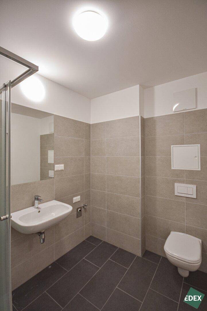 Funktionales Badezimmer mit wandhängendem WC, Waschbecken und modernen Fliesen an Wänden und Boden.