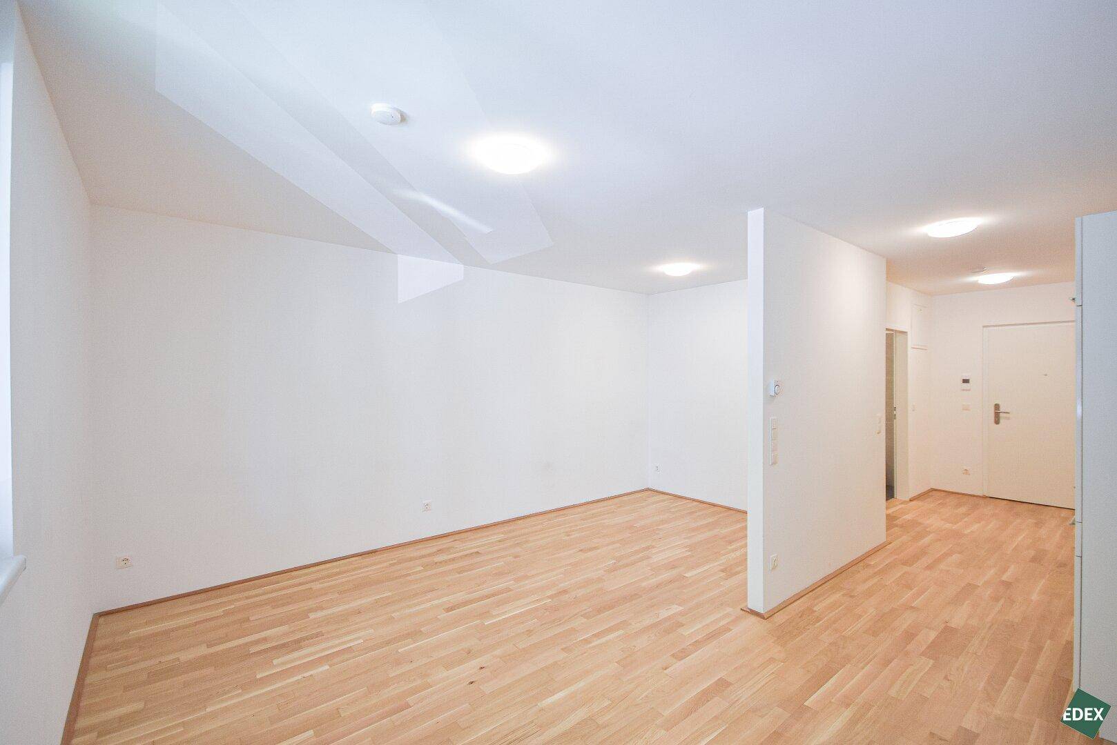 Geräumiger Wohnbereich mit hellem Parkettboden und Zugang zum Eingangsbereich der Wohnung.