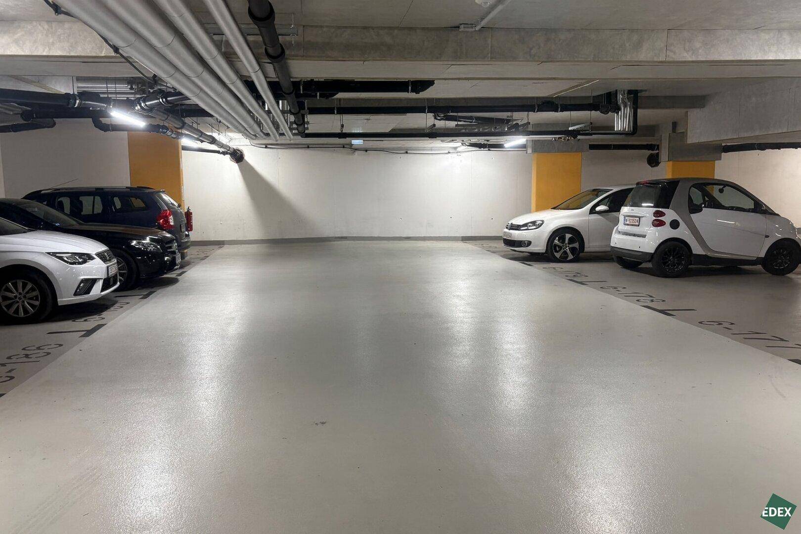 Tiefgarage mit markierten Stellplätzen und mehreren geparkten Fahrzeugen, gut beleuchtet.