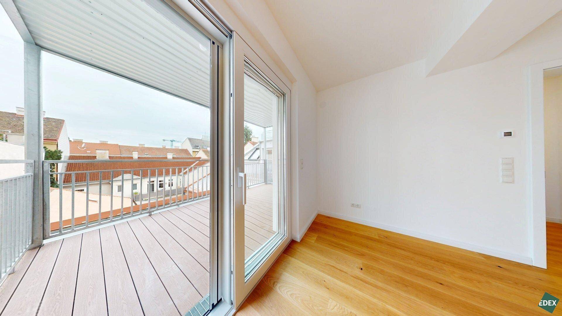 Geräumiger Balkon mit Holzdielen und Blick über die Dächer der umliegenden Gebäude.