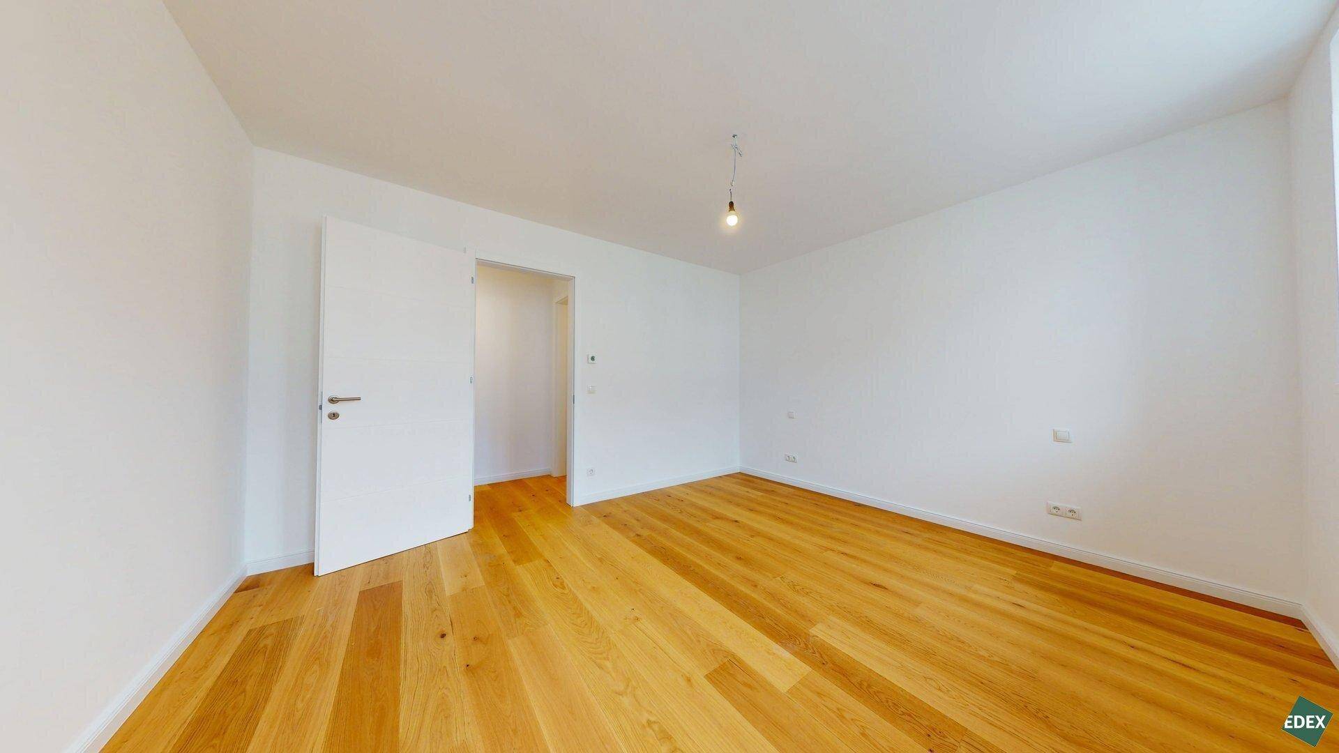 Geräumiges, helles Zimmer mit Holzboden und weiß gestrichenen Wänden, ideal als Schlafzimmer.