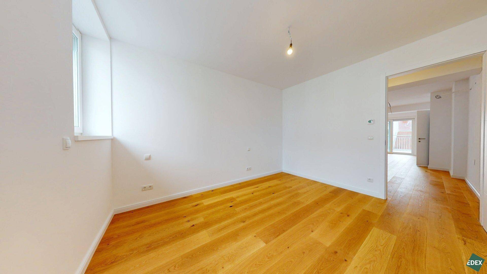 Helles Zimmer mit Holzboden und einem Fenster, das einen Blick nach draußen ermöglicht.
