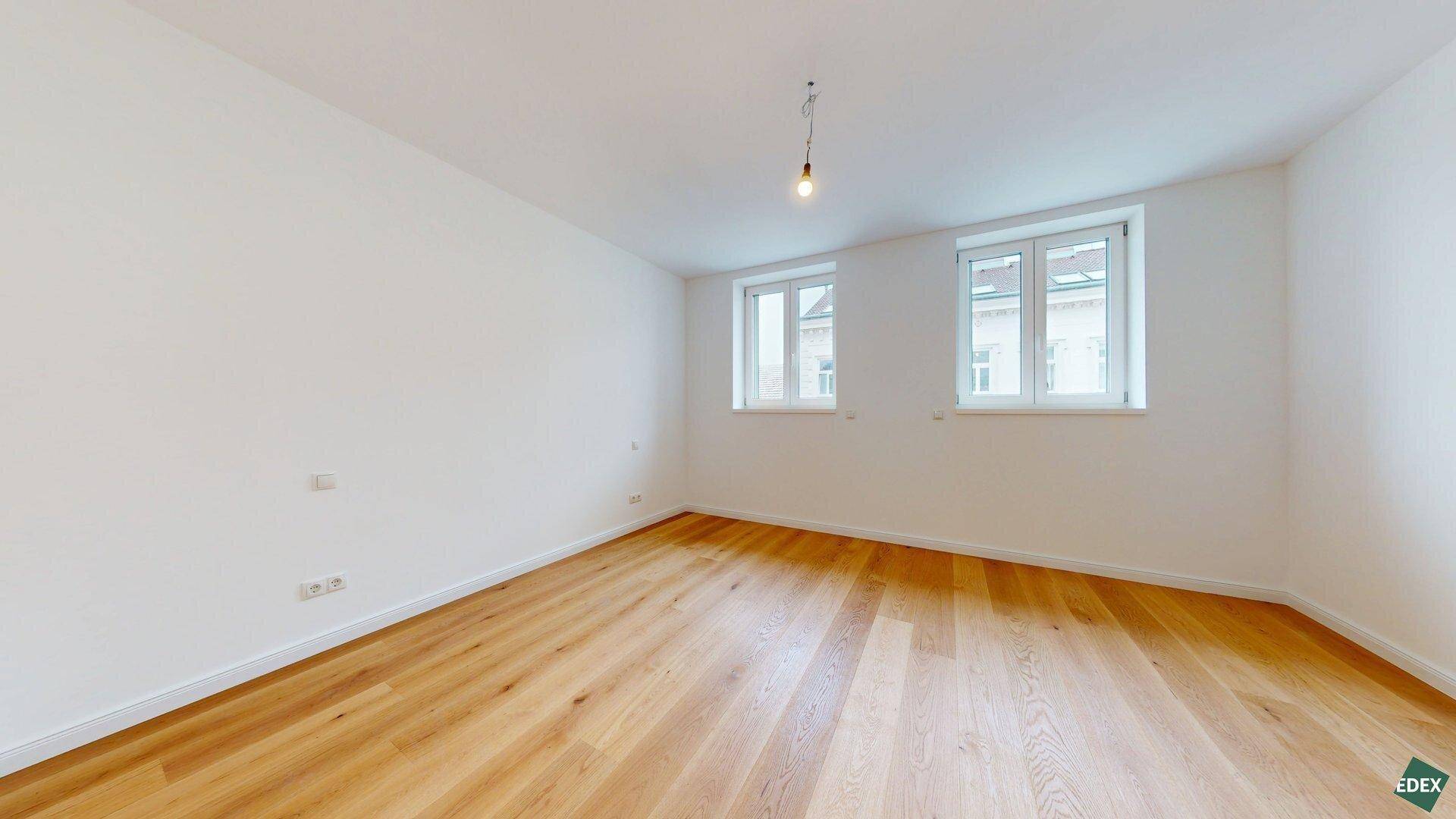 Lichtdurchflutetes Zimmer mit Holzboden und zwei Fenstern, perfekt als Schlaf- oder Arbeitszimmer.